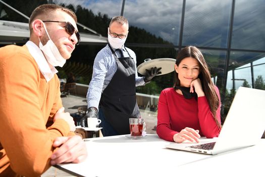 coronavirus outbreak Group of casual business People in outdoor restaurant wearing protective medical mask, business team collaborating and brainstorming business ideas  while working on laptop