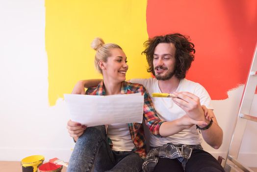 Happy young couple relaxing after painting a room in their new house on the floor