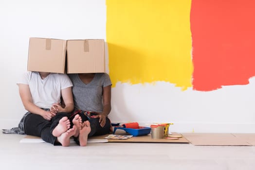 Happy young multiethnic couple relaxing and playing with cardboard boxes after painting a room in their new house on the floor