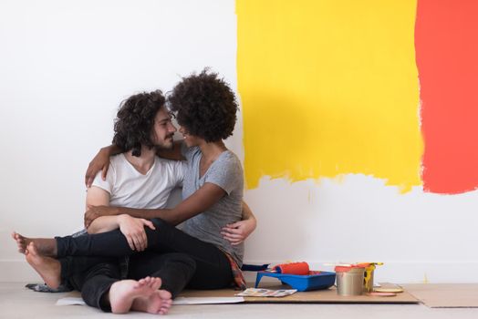 Happy young multiethnic couple relaxing after painting a room in their new house on the floor