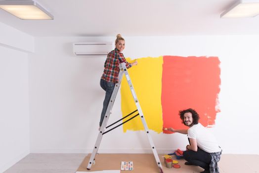 happy smiling young couple painting interior wall of new house