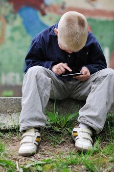 young blonde boy playing videogames outdoor in park