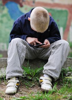 young blonde boy playing videogames outdoor in park