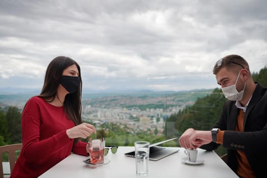 coronavirus outbreak Group of casual business People in outdoor restaurant wearing protective medical mask, business team collaborating and brainstorming business ideas  while working on laptop