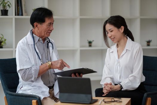 Senior asian doctor physician consulting young female patient, talking to client at medical checkup visit. Geriatric diseases treatment. Elderly medical health care concept