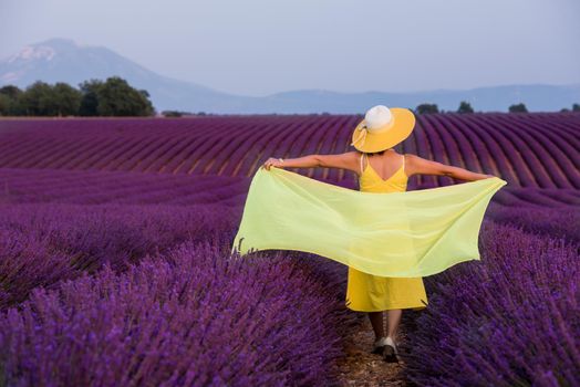 beautiful young asian woman in yellow dress and hat relaxing and having fun on purple flower lavender field