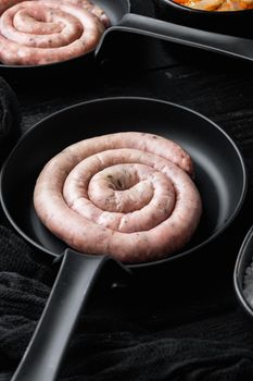 Raw spiral sausage set in cast iron frying pan, on black wooden table background