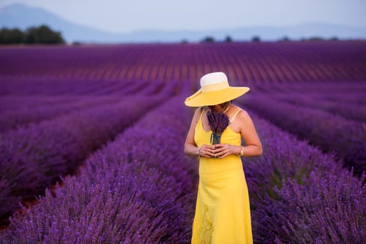 beautiful young asian woman in yellow dress and hat relaxing and having fun on purple flower lavender field