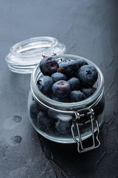 Ripe blueberry in glass jar, on black background.