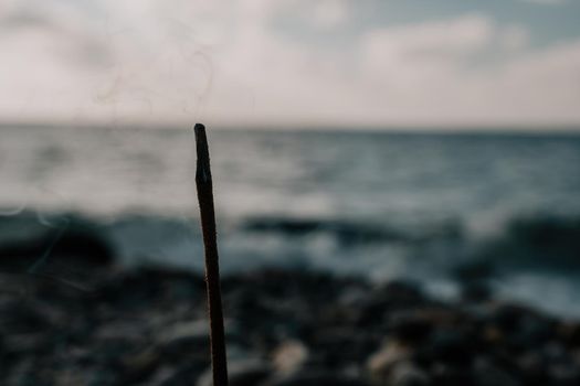 Close up of incense aroma stick burning on the sea shore. Meditation concept. Morning sea waves washing plate with aroma stick.