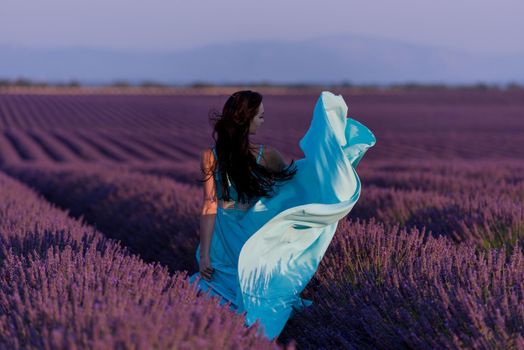 beautiful young woman in cyand dress relaxing and having fun on wind in purple lavander flower field