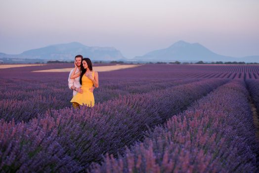 young loving couple having romantic time hugging and kissing on purple lavender flower field in sunset