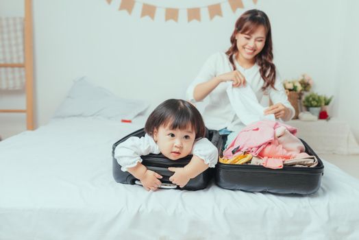 mother prepares clothes to put in her suitcase and her daughter plays with her suitcase