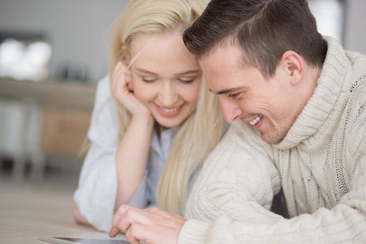 Young Couple on the floor in front of fireplace surfing internet using digital tablet on cold winter day