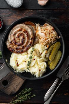 Fried Bavarian German Nürnberger sausages with sauerkraut, mashed potatoe in cast iron frying pan, on old dark wooden table background