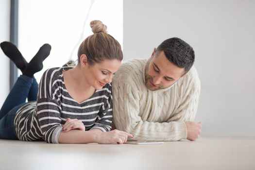 Young Couple on the floor in front of fireplace surfing internet using digital tablet on cold winter day