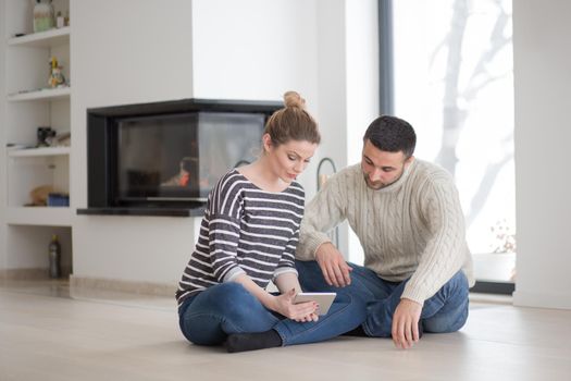 Young Couple on the floor in front of fireplace surfing internet using digital tablet on cold winter day