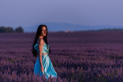 portrait of a beautiful young woman in cyand dress relaxing and having fun on wind at purple lavander flower field