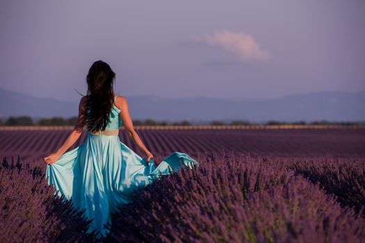 beautiful young woman in cyand dress relaxing and having fun on wind in purple lavander flower field