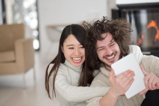 beautiful young multiethnic couple using tablet computer in front of fireplace on cold winter day at home