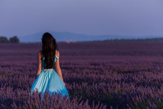 beautiful young woman in cyand dress relaxing and having fun on wind in purple lavander flower field