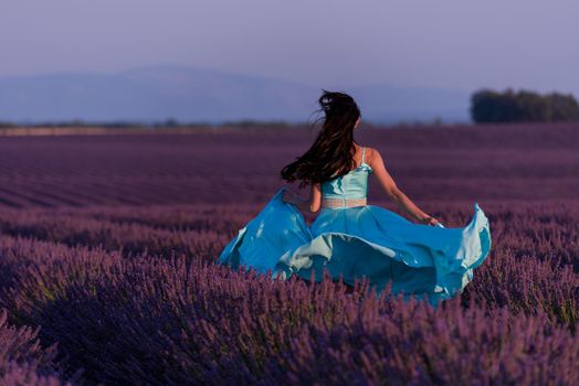 beautiful young woman in cyand dress relaxing and having fun on wind in purple lavander flower field