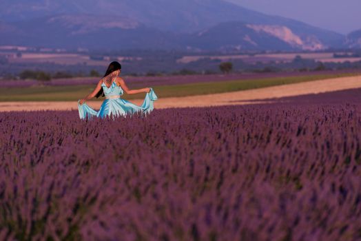 beautiful young woman in cyand dress relaxing and having fun on wind in purple lavander flower field