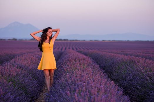 beautiful young woman in yellow dress relaxing and having fun on purple flower lavander field