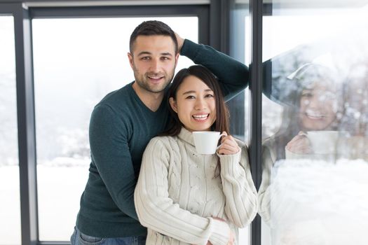 happy young multiethnic couple enjoying morning coffee by the window on cold winter day at home