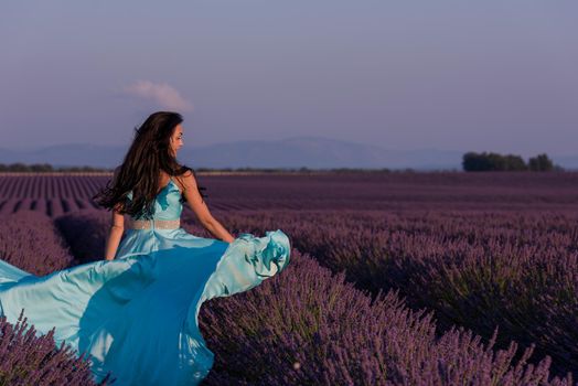 beautiful young woman in cyand dress relaxing and having fun on wind in purple lavander flower field