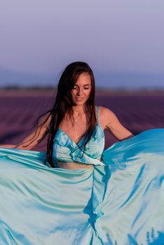 portrait of a beautiful young woman in cyand dress relaxing and having fun on wind at purple lavander flower field