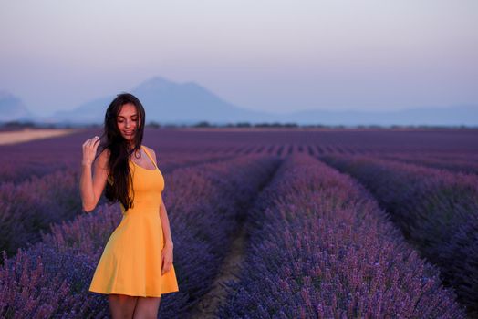 beautiful young woman in yellow dress relaxing and having fun on purple flower lavander field