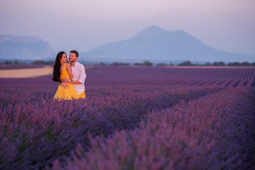 young loving couple having romantic time hugging and kissing on purple lavender flower field in sunset