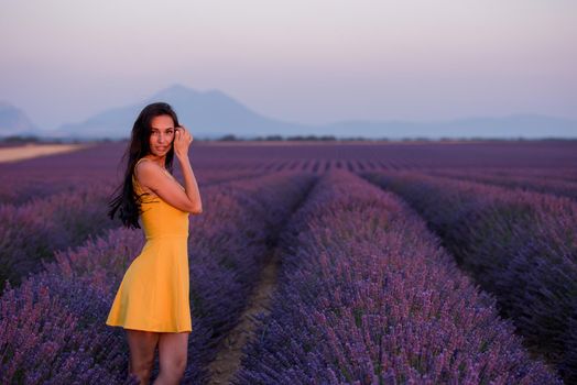 beautiful young woman in yellow dress relaxing and having fun on purple flower lavander field