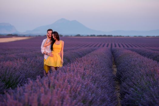 young loving couple having romantic time hugging and kissing on purple lavender flower field in sunset