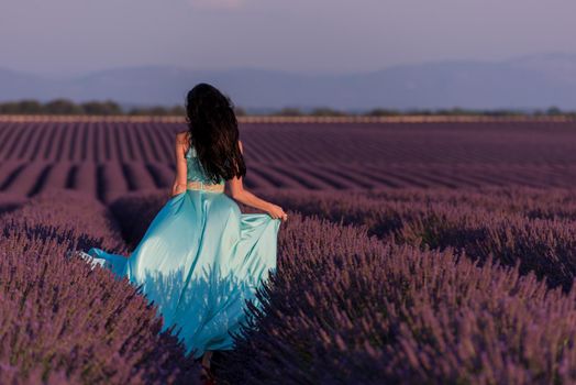 beautiful young woman in cyand dress relaxing and having fun on wind in purple lavander flower field