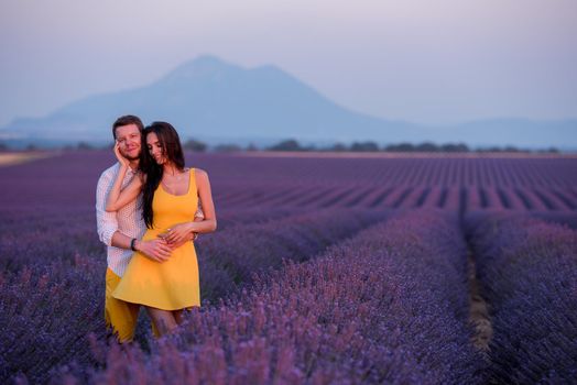 young loving couple having romantic time hugging and kissing on purple lavender flower field in sunset