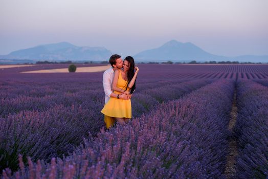 young loving couple having romantic time hugging and kissing on purple lavender flower field in sunset