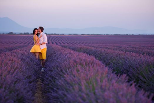 young loving couple having romantic time hugging and kissing on purple lavender flower field in sunset