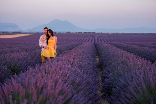 young loving couple having romantic time hugging and kissing on purple lavender flower field in sunset