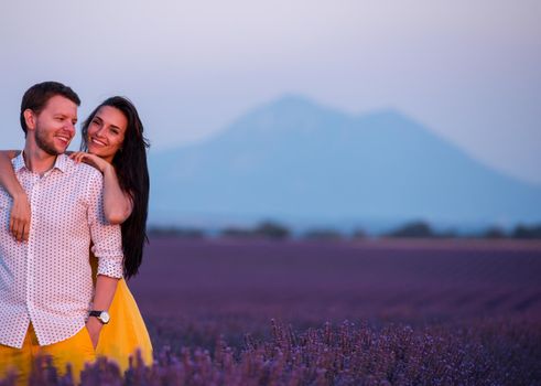 young loving couple having romantic time hugging and kissing on purple lavender flower field in sunset