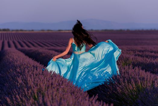 beautiful young woman in cyand dress relaxing and having fun on wind in purple lavander flower field