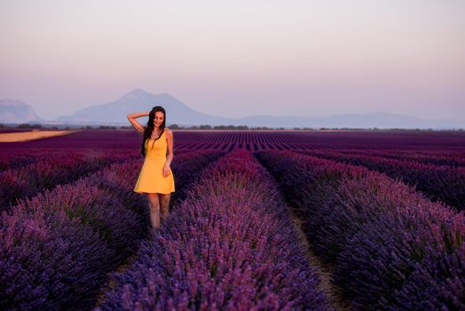 beautiful young woman in yellow dress relaxing and having fun on purple flower lavander field