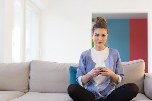 young happy woman using mobile phone on sofa at luxury home