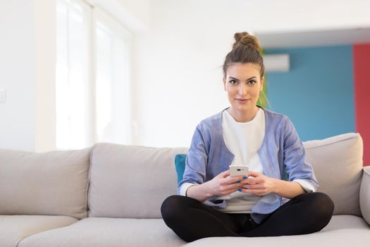 young happy woman using mobile phone on sofa at luxury home