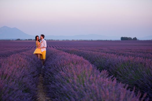 young loving couple having romantic time hugging and kissing on purple lavender flower field in sunset