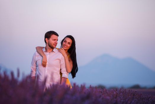 young loving couple having romantic time hugging and kissing on purple lavender flower field in sunset