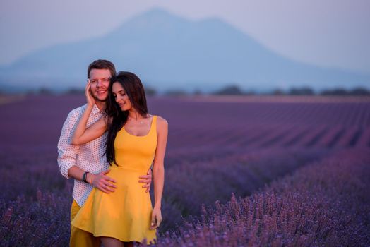 young loving couple having romantic time hugging and kissing on purple lavender flower field in sunset