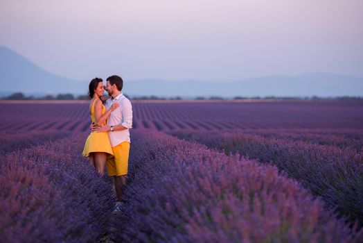 young loving couple having romantic time hugging and kissing on purple lavender flower field in sunset