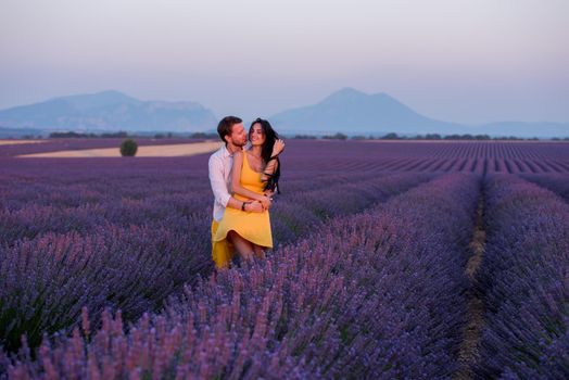 young loving couple having romantic time hugging and kissing on purple lavender flower field in sunset